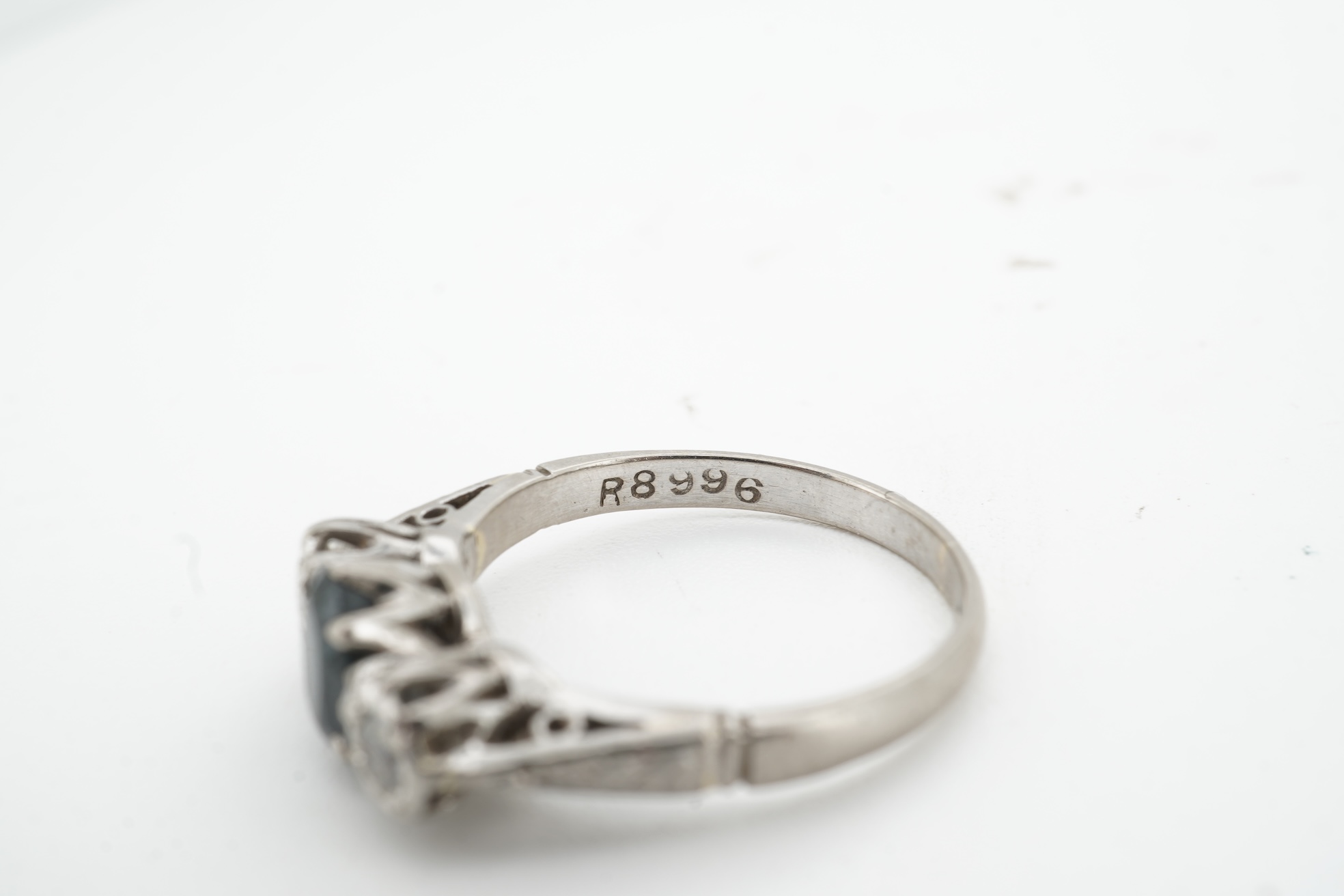 A sapphire and diamond ring, claw-set with an oval sapphire measuring approximately 6.2 x 4.5 x 3.2mm, between shoulders set with brilliant-cut diamonds totalling approximately 0.14 carats, mounted in platinum and pallad